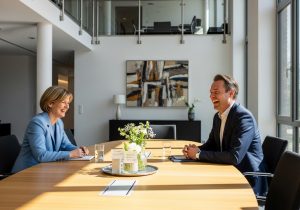 Zwei Menschen sitzen bei einer Verhandlung, lachen entspannt und zeigen gegenseitiges Vertrauen am Tisch.